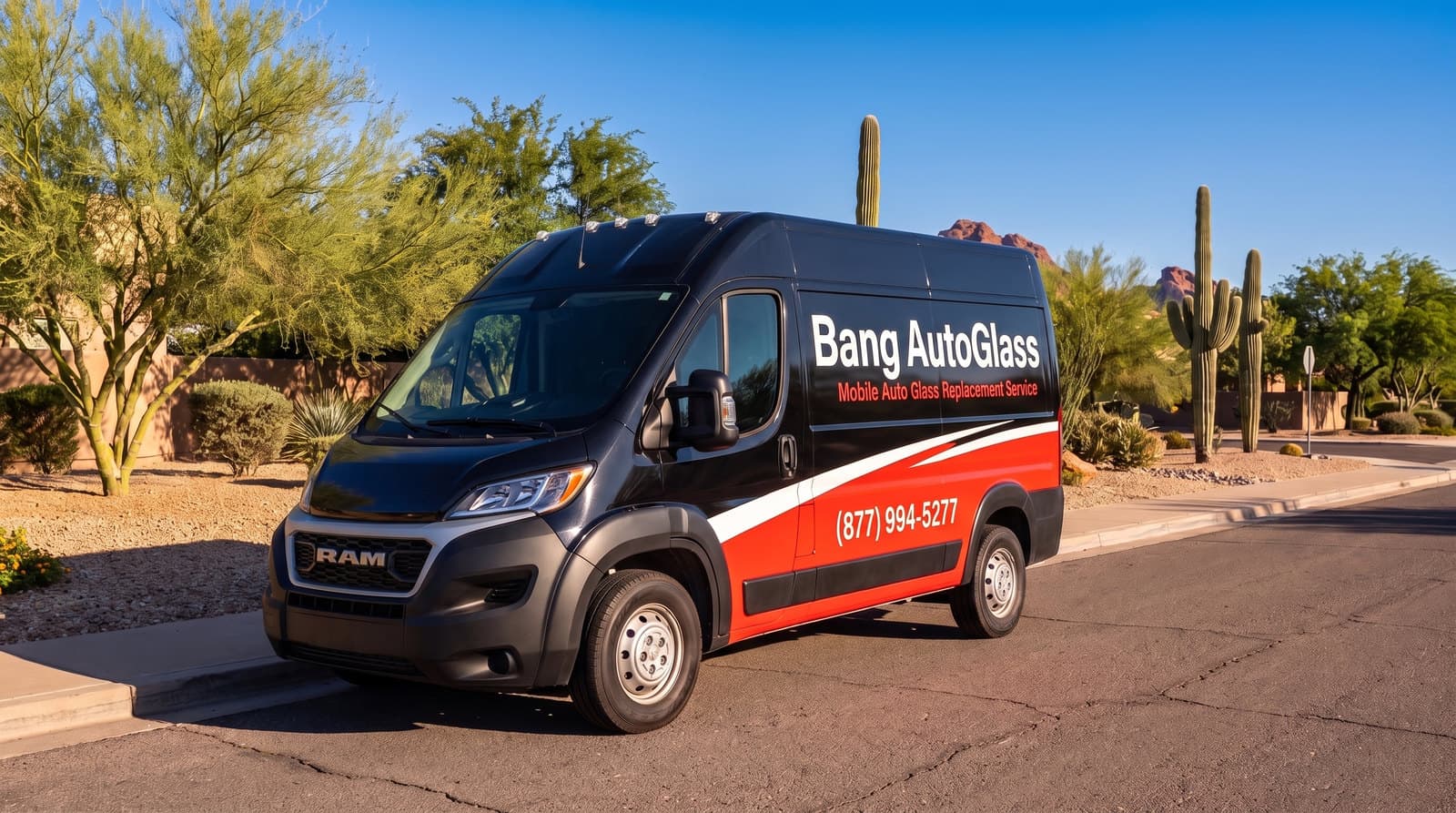Red-and-black van with the Bang AutoGlass logo on a sunny desert street with saguaro cacti and red-rock mountains