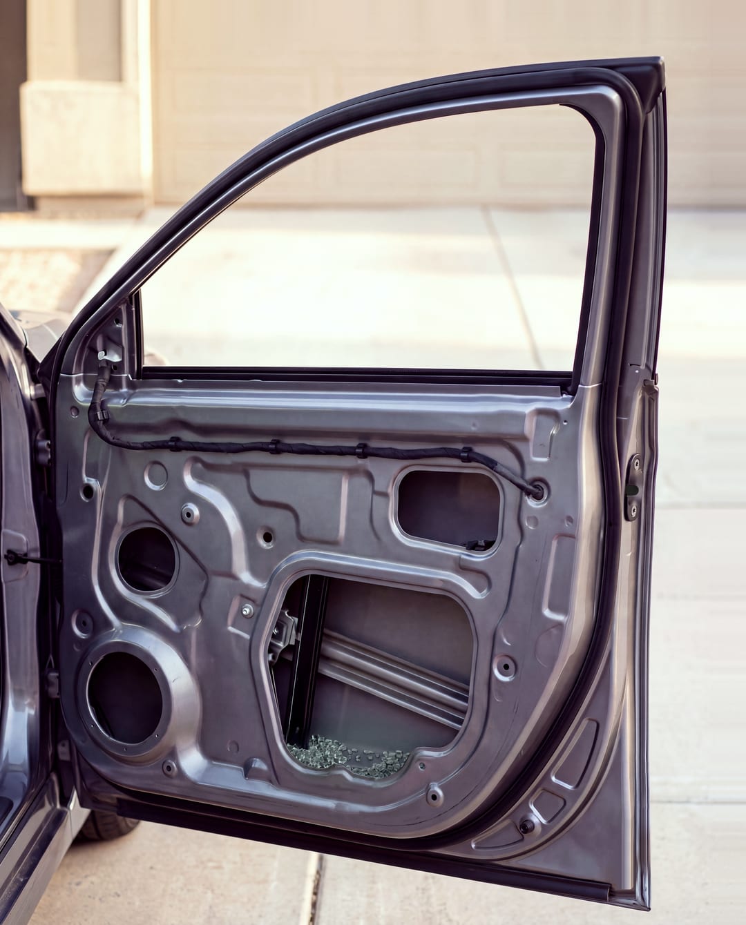 Inside a car door with the trim panel off: the window track and the bottom of the door, where small cubes of broken tempered glass have collected.