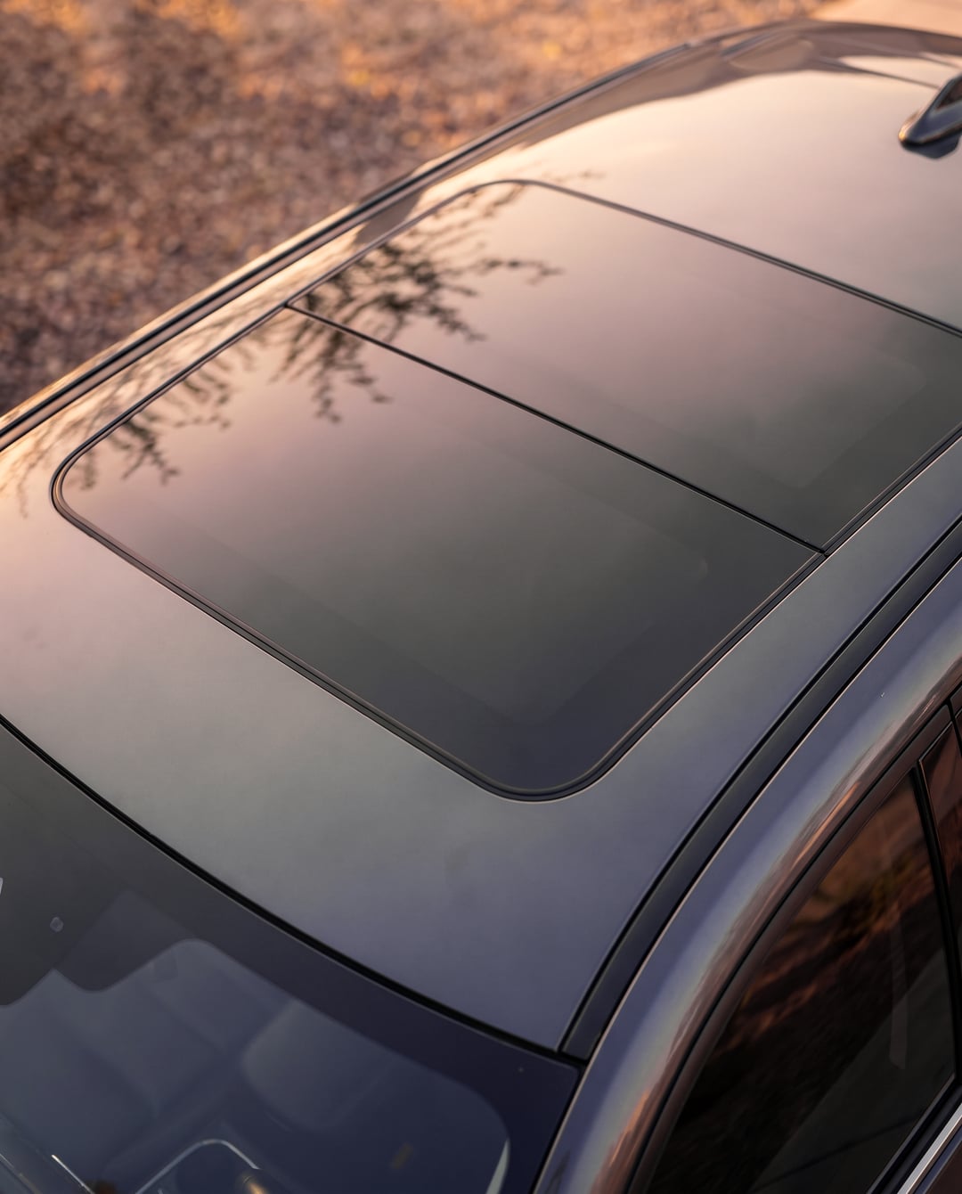 Primer plano del techo de vidrio de una SUV oscura al atardecer, con el panel delantero cerrado al ras del techo.